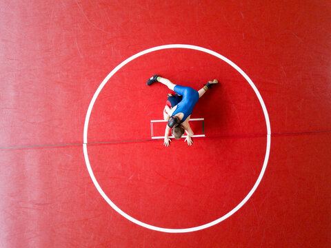 Aerial View Of Two Wrestlers Competing On A Red Wrestling Mat. 