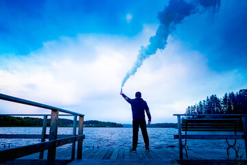A man calls for help. A young man with a smoke bomb in his hand on the background of the lake....