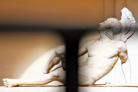 Marble statue of a lying warrior. Image seen through an iron grate