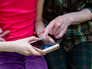 Young cute granddaughter helping grandmother to use the phone. Close-up of the hands of the grandmother and granddaughter.