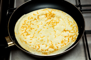 cooking pancakes in a pan on a gas stove. female hand pours the batter into the pan.