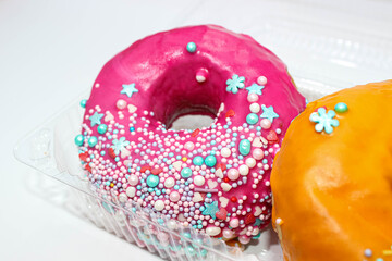 Two delicious American doughnuts in a transparent container decorated with decorative sprinkles.