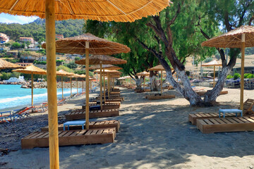 Empty sun loungers without people under straw umbrellas on the beach.