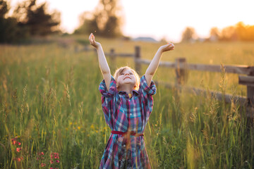 Naklejka na ściany i meble Happy child raising hands to the sky, summer sunset in field, concept of happy childhood, innocence and peace