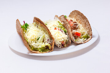 3 tacos . Mexican food created with tortillas, cream cheese, cooked chopped meat, avocado sauce, lettuce, and tomato salad, with cheese on top. white background
