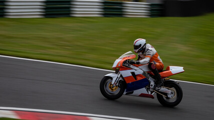 Obraz na płótnie Canvas A panning shot of an orange and white racing bike as it circuits a track