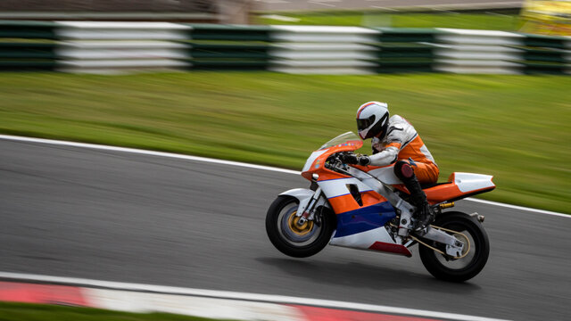 A panning shot of an orange and white racing bike on one wheel as it circuits a track