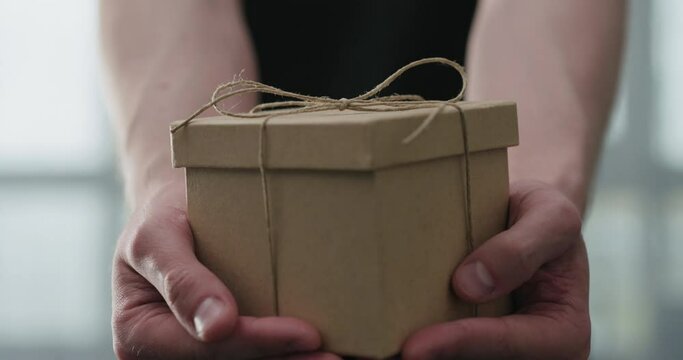 Slow motion young man shows brown craft paper gift box
