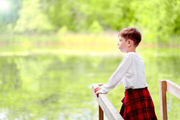 Naklejka premium a boy stands on a bridge by the lake. Summer day on the river. Blue Lake.