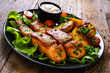 Fried salmon steak with potatoes and vegetables served on black plate on wooden table