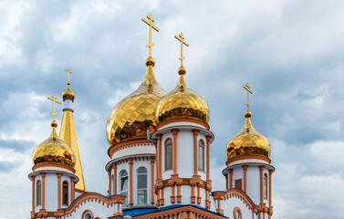 Fototapeta na wymiar Golden domes of a snow-white Christian church against a disturbing cloudy blue summer sky