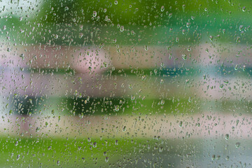 Defocused photography of city street in rainy sunset. Concepts of beauty of city in rain. View through window. Water drops at the window glass