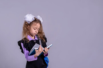 Schoolgirl with ribbons in school uniform holding a book on a gray background, copy space.