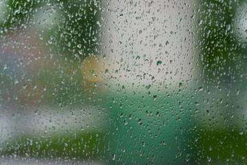 Defocused photography of city street in rainy sunset. Concepts of beauty of city in rain. View through window. Water drops at the window glass
