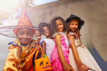 Boy with candy bucket over group of kids in Halloween costumes hug standing together and smiling looking at camera