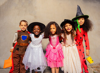 Group of kids in Halloween costumes hug standing together and smiling looking at camera