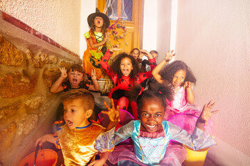 Many diverse looking kids in Halloween costumes sit on the stairs of the door of the house