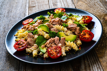 Pasta with tuna, avocado and cherry tomatoes served on black plate on wooden table