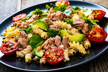 Pasta with tuna, avocado and cherry tomatoes served on black plate on wooden table