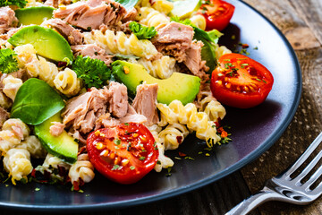 Pasta with tuna, avocado and cherry tomatoes served on black plate on wooden table