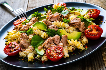Pasta with tuna, avocado and cherry tomatoes served on black plate on wooden table