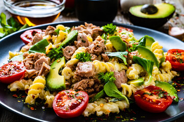 Pasta with tuna, avocado and cherry tomatoes served on black plate on wooden table