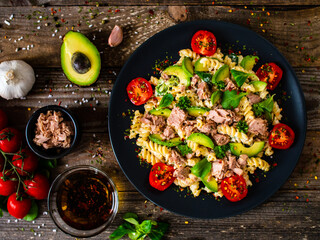 Pasta with tuna, avocado and cherry tomatoes served on black plate on wooden table