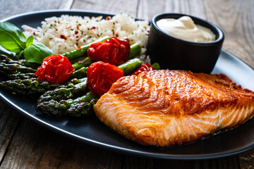 Fried salmon steak with rice and asparagus served on black plate on wooden table
