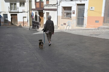 An elder woman walks with her dog through an alley in a small spanish town called Finestrat. Activities in the corona-time.