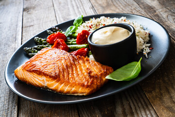 Fried salmon steak with rice and asparagus served on black plate on wooden table
