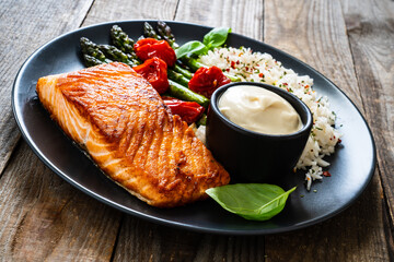 Fried salmon steak with rice and asparagus served on black plate on wooden table
