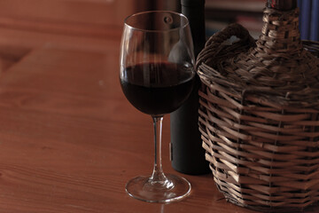 old wicker jerrycan of wine with its bottle and glass of wine on wooden table
