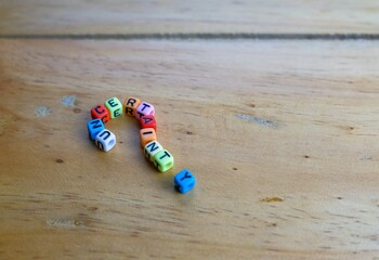 Alphabet beads UNCERTAINTY in question mark shape on wooden table. Selective focus.