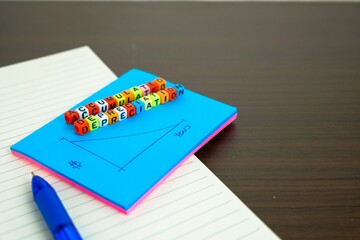 Conceptual of accumulated depreciation in financial statements. Colorful alphabet beads stacked forming the words over dark table. On spiral sticky note, note book and pen visible.