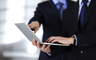 Business people discussing a presentation at meeting, standing in a modern office. Unknown businessman with a colleague search for some information at the laptop, lawyers at negotiation. Teamwork and