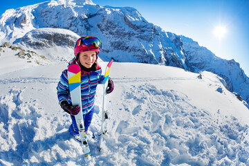 Fototapeta na wymiar Full height portrait from side of smiling skier girl with ski standing in snow over mountain summit view wear pink mask and color glasses