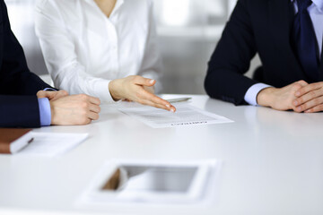 Group of business people, men and a woman, discuss details of a contract at meeting in a modern office. Discussion at negotiation or workplace. Teamwork, partnership and business concept