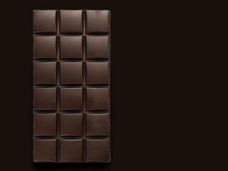 A bar of dark chocolate on a dark background.