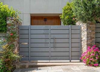 elegant family house entrance metallic grey door by the sidewalk with plenty of foliage and flowers