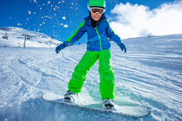 Fototapeta na wymiar Active boy move fast on snowboard throwing snow around - close motion image over blue sky and ski slope