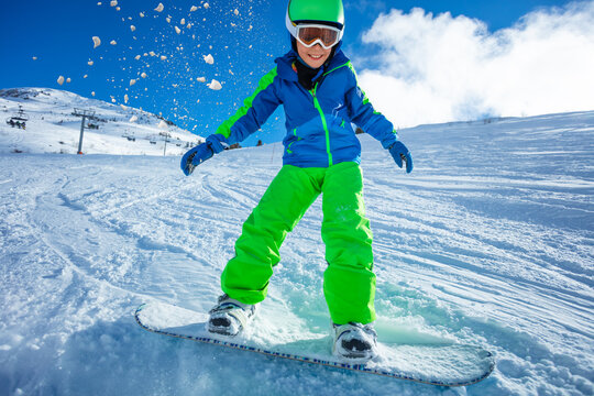 Active boy move fast on snowboard throwing snow around - close motion image over blue sky and ski slope