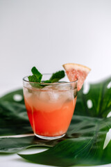 Grapefruit cocktail, lemonade with lime, mint and pieces of ice on a green tropical leaf.