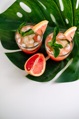 Grapefruit cocktail, lemonade with lime, mint and pieces of ice on a green tropical leaf.