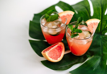 Grapefruit cocktail, lemonade with lime, mint and pieces of ice on a green tropical leaf.