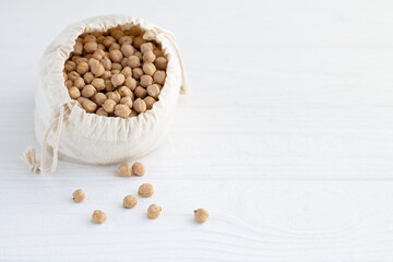 Close-up of raw chickpeas in linen eco bag on white wooden table with copy space