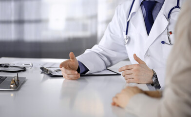 Unknown male doctor and patient woman discussing something while sitting in clinic and using clipboard. Best medical service in hospital, medicine, pandemic stop