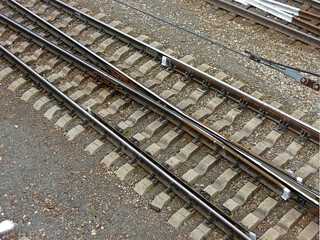 Fototapeta premium Side view onto railroad tracks. Construction of tracks consist of steel rails, installed on ties (sleepers) & ballast, on which rolling stock, usually fitted with metal wheels, moves