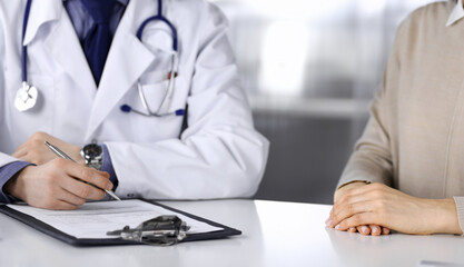 Unknown male doctor and patient woman discussing something while sitting in clinic and using clipboard. Best medical service in hospital, medicine, pandemic stop