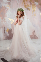 Portrait of a young beautiful woman in wedding dress with wreath and bouquet of fresh flowers.