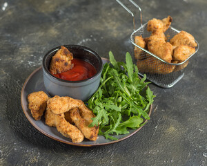 Chicken nuggets on a plate with herbs and tomato sauce and in a deep-frying basket horizontal arrangement